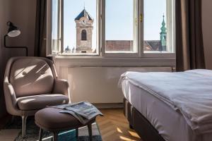 维也纳维也纳老城小型豪华酒店的一间卧室配有一张床和一把椅子,还有一个钟楼