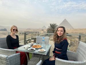 开罗Blue Scarab Pyramids View的两个女人坐在金字塔前的桌子上