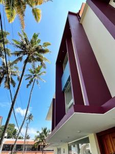 瓦尔卡拉BAVA Lalitha Retreat Center Varkala的一座紫色的建筑,背后是棕榈树