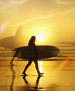 梅森堡Cape Capsules的一名妇女带着冲浪板在海滩上行走
