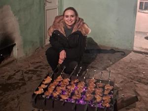 XınalıqXinaliq İzzet's Riverside Home Stay的女人坐在烤架旁边,烤盘上摆着糕点