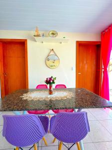 帕罗卡Casa de Anita Pinheira 30m da praia的一张带紫色椅子的桌子和一个带鲜花的花瓶