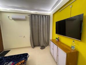 BhauliCozzy Inn的一间起居室,在黄色的墙上配有平面电视。