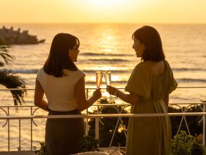 读谷村Umi No Terrace Yomitan Toya的两名妇女站在阳台上,拿着酒杯