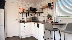 TamahereRustling Oaks NZ Tropical Tiny House的小厨房配有白色橱柜和桌椅