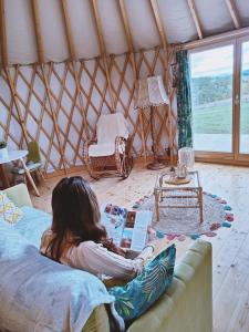 WolanyGlamping Niebiańska Osada Jurty Dolnośląskie & SPA的坐在蒙古包沙发上读书的女人