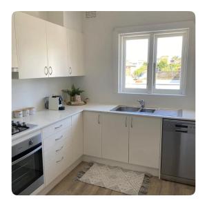 悉尼Little Manly Getaway的厨房配有白色橱柜、水槽和窗户。