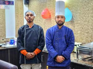 西姆拉Hotel Taj Palace near Mall Road的两个男人站在厨房里,戴着厨师帽