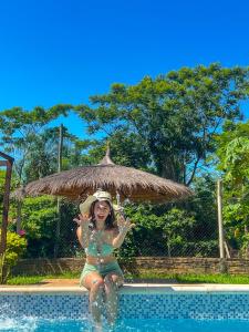 ItauguáLa Casita de Aregua的坐在游泳池的一只草伞下的女孩