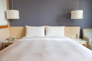 高雄康桥商旅 - 光荣码头的一张带白色床单的床、两张桌子和两盏灯