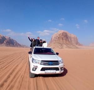 瓦迪拉姆Shakria Bedouin Life Camp的一群人站在沙漠中的一辆白色汽车上