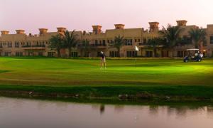 拉斯阿尔卡麦Al Hamra Village Hotel的站在一座大楼前的高尔夫球场上的人