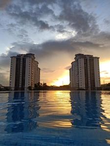 吉隆坡Suria Kipark Damansara 3R2B 950sq ft Apartment的日落时分在两栋公寓楼前的游泳池