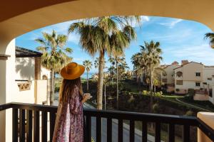 米哈斯科斯塔Wyndham Grand Costa del Sol的站在一个眺望棕榈树的阳台的戴帽子的女人