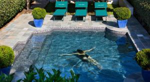 厄尔巴隆加Demeure Castel Brando Hôtel & Spa的一位女士在带椅子的游泳池游泳