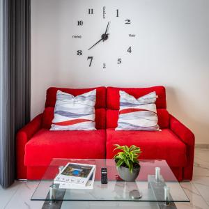 圣朱利安斯Urban Downtown Den in St Julians的红色的沙发,配有枕头,墙上挂着一个钟