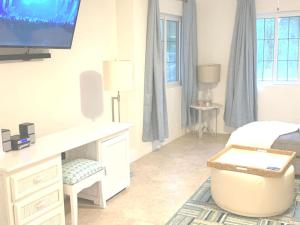 罗克桑德Suites Pineapple的白色卧室配有书桌和墙上的电视