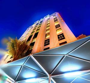 科威特布拉沃皇家套房酒店 的一座高大的建筑,前面有一棵棕榈树