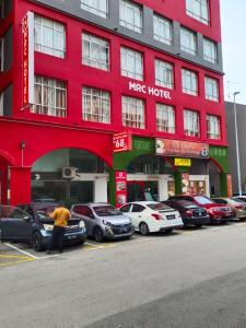 马六甲MRC Hotel Melaka Raya的站在红色建筑前面,有停车车的人