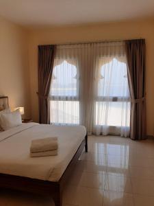 拉斯阿尔卡麦Hala Holiday Homes- Bab Al Bahr Residence, Al Marjan Island的一间卧室设有一张床和两个大窗户