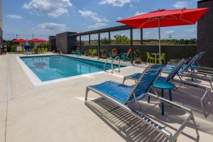 彭萨科拉Tru By Hilton Pensacola Airport Medical Center的一个带蓝色椅子和红色遮阳伞的游泳池