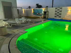 米多恩Villa luxe calme djerba的旁边设有一张桌子和椅子的绿色游泳池