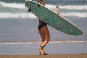 塔哈佐特Welle Surf Morocco的一名妇女带着冲浪板在海滩上行走