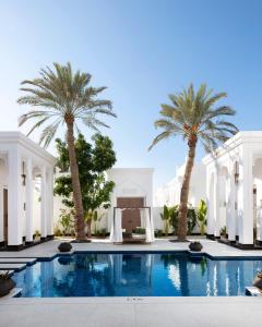 麦纳麦Raffles Al Areen Palace Bahrain的一座楼前种有棕榈树的游泳池