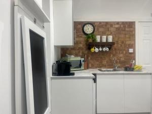 卢顿Nice and Cosy Large Studio near Luton Airport的厨房配有白色橱柜和砖墙上的时钟