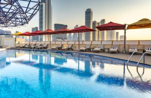 迪拜Leva Hotel and Suites, Opposite Downtown的一个带红色遮阳伞的游泳池,并享有城市天际线