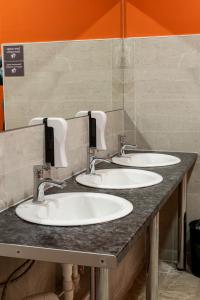 比什凯克People Hostel & Coworking的公共浴室设有3个水槽和橙色墙壁