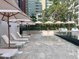 曼谷Floral Court Hotel & Residence Sukhumvit 13的一个带椅子和遮阳伞的庭院和一个游泳池