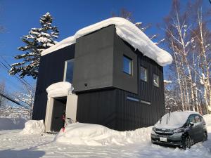 二世古NISEKO EPIC HOUSE的雪中停放一辆汽车的黑房子