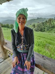 Ban Mae Pan Noiบ้านพักชิปู ป่าบงเปียง的一位年纪较大的女人坐在长凳上,头上戴着绿色帽子