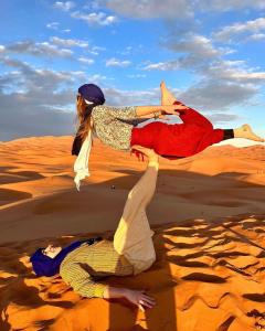El GoueraChegaga Regency Camp的两个人躺在沙漠的沙子里