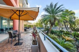 达尔文Resort Style City View King Bed Pool Balcony的阳台配有遮阳伞和椅子,并种植了棕榈树。