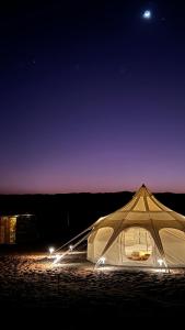 BadīyahSafari Infinity Camp的夜晚坐在沙子里的白色帐篷