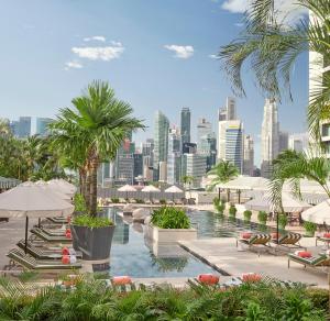 新加坡Mandarin Oriental, Singapore的一个带椅子和遮阳伞的游泳池,并享有城市天际线
