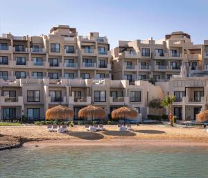 赫尔格达Creek Hotel and Residences El Gouna的海滩上一座带稻草遮阳伞的大型建筑