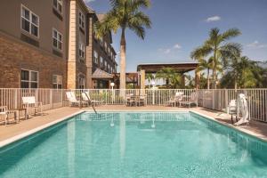 布雷登顿Country Inn & Suites by Radisson, Bradenton-Lakewood-Ranch, FL的一个带椅子的游泳池、一座建筑和棕榈树