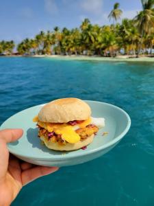 El PorvenirSan Blas Sailing Experience With Us!的手持盘子,在海滩上吃早餐三明治