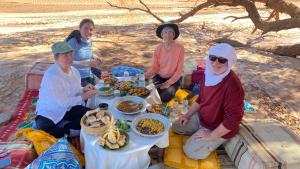 El GoueraAtta Desert Camp的一群人坐在桌子旁吃着食物