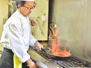 茅野Petit Hotel Kanan的厨师在烤架上用锅烹制食物