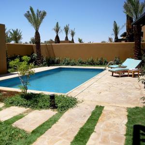 利雅德Aseel Resort的一个带长凳和棕榈树的庭院内的游泳池