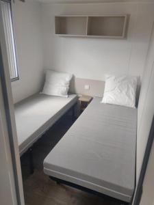 塞里尼昂Super mobil-home aux Sables du Midi的小客房内的两张床,配有白色床单和枕头