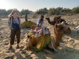 斋沙默尔Hotel Pol Haveli Jaisalmer的一位妇女站在海滩上的骆驼旁边