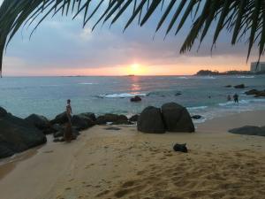 乌纳瓦图纳Happy Beach Villa Resort的站在海滩上,在海洋中日落的男人