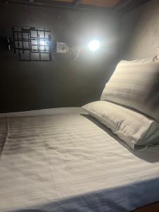 清迈Eachother Hostel的一张铺有白色床单的床和墙上的灯