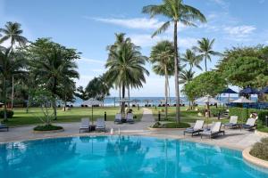 芭东海滩Phuket Marriott Resort & Spa, Merlin Beach的一个带椅子和棕榈树的游泳池以及大海