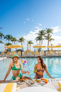 迈阿密海滩纽波特海滨度假酒店的两个比基尼女人坐在游泳池的桌子上